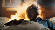 An AI-generated version of the filmmaker John Carpenter sits in a living room on fire.